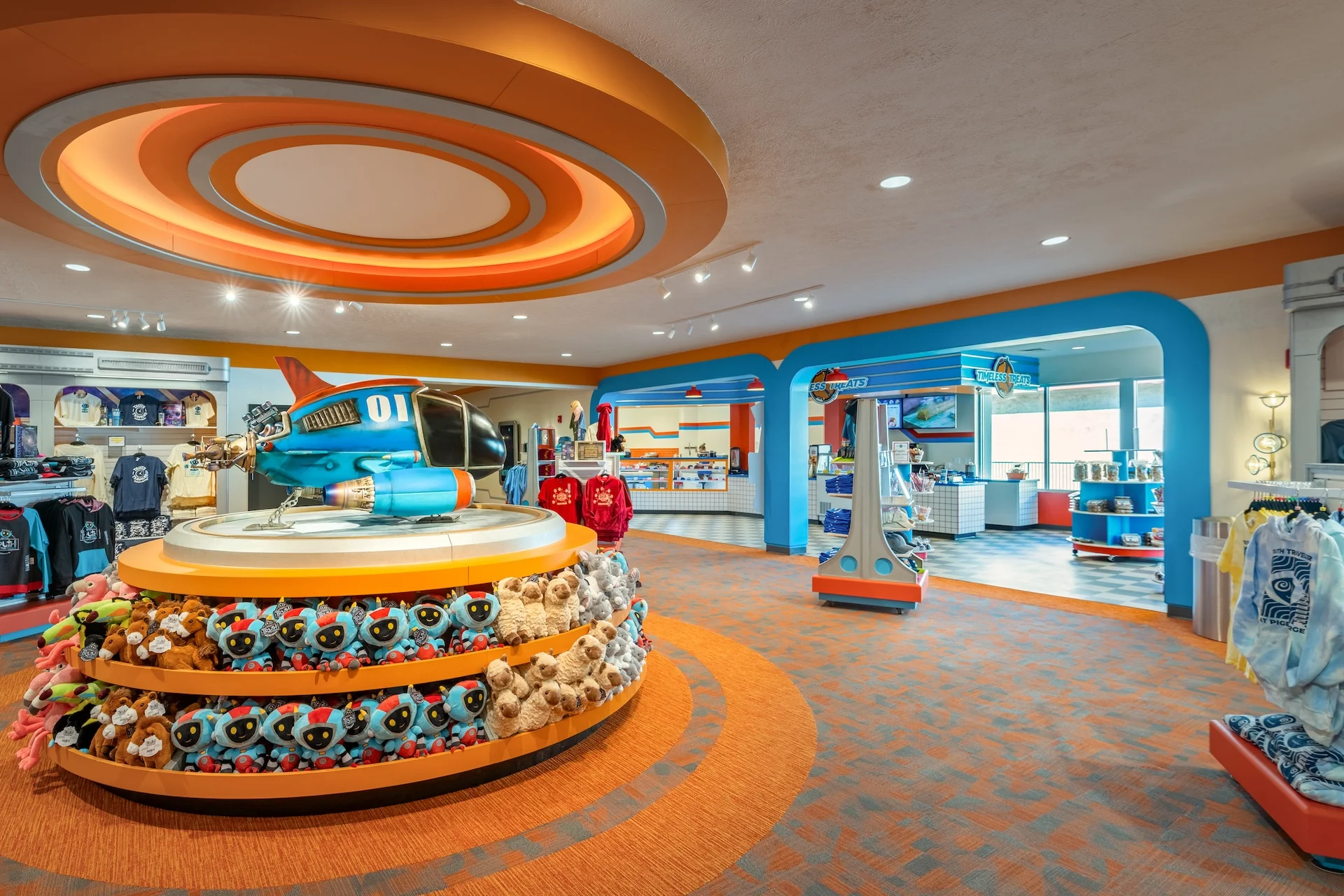 Colorful retail space featuring a blue and orange themed display with a model aircraft, surrounded by plush toys on circular shelves, showcasing merchandise in a vibrant shopping environment designed for immersive experiences.