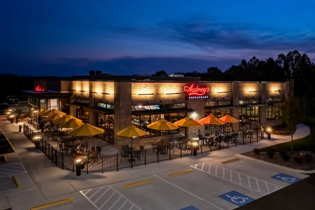 Aubrey's restaurant in Lenoir City, Tennessee, featuring a modern exterior with bright yellow umbrellas, warm lighting, and a welcoming ambiance, designed and built by GAE Architecture + Design, a top commercial architect firm in Knoxville, TN.
