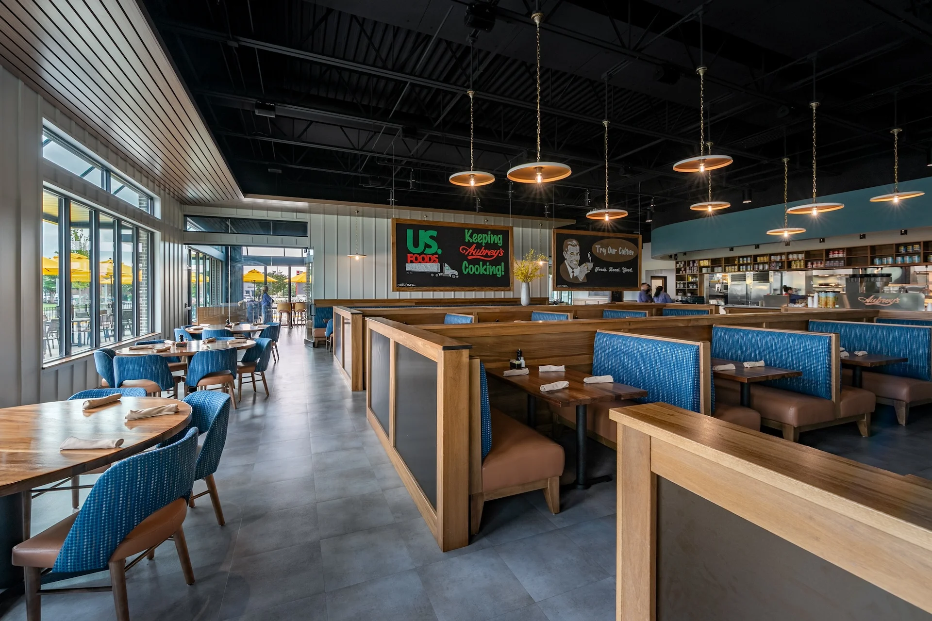 Interior view of Aubrey's restaurant in Lenoir City, featuring deep blue upholstery, warm wood tones, and modern pendant lighting, designed by GAE Architecture + Design, showcasing a blend of contemporary style and established brand identity.