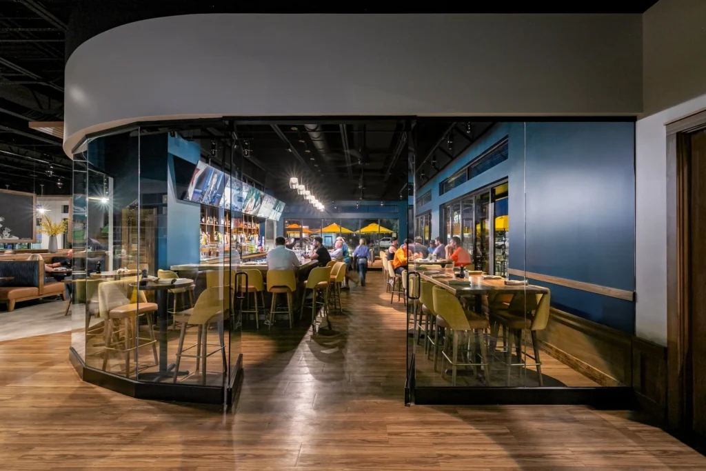Interior view of Aubrey's restaurant in Lenoir City, featuring a modern bar area with glass walls, deep blue accents, and warm wood tones, designed and built by George Ewart, a top commercial architect firm in Knoxville, TN.