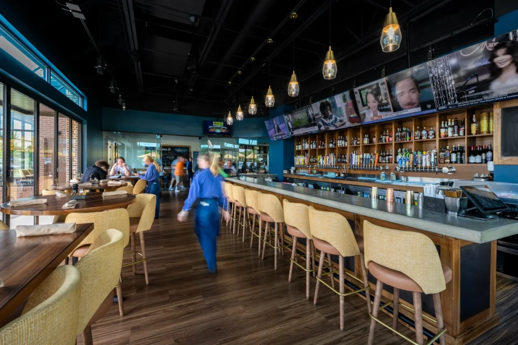 Interior view of Aubrey's restaurant in Lenoir City, showcasing a modern bar area with pendant lighting, a variety of beverages, and patrons enjoying the space, designed and built by George Ewart, a top commercial architect firm in Knoxville, TN.