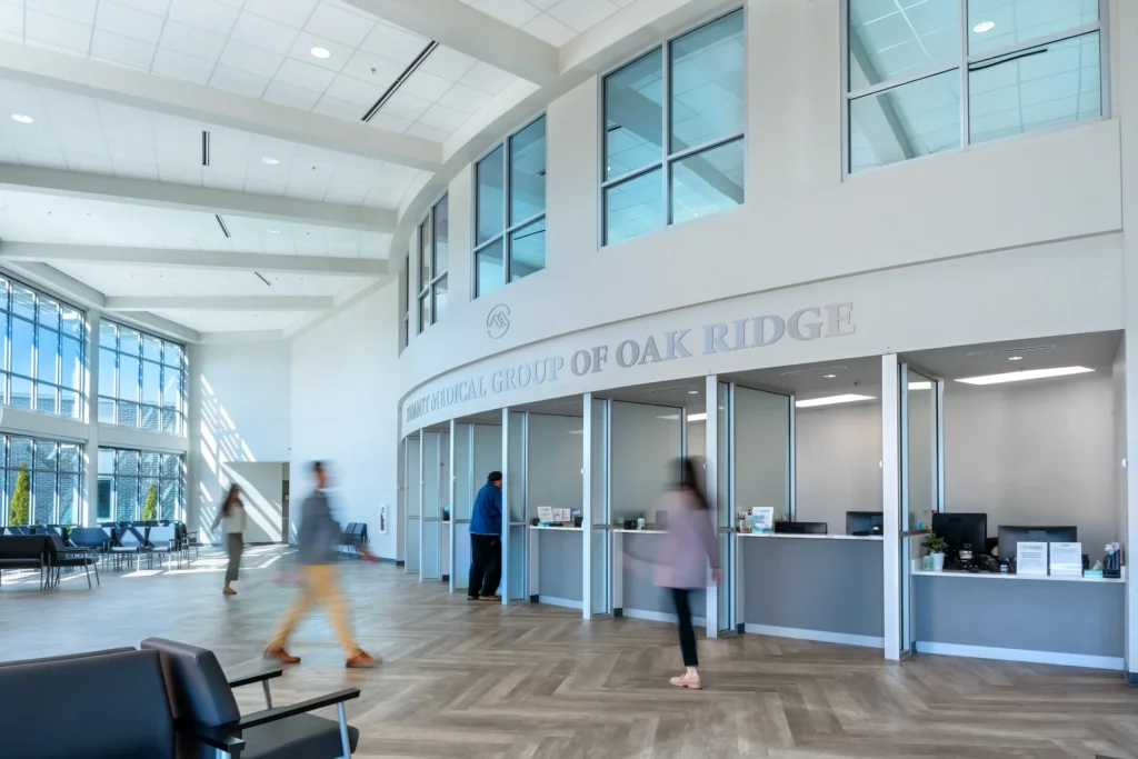 Modern atrium lobby of Summit Medical Group in Oak Ridge, Tennessee, featuring large windows, reception area, and patients and staff interacting, designed and built by George Ewart, a top commercial architect firm in Knoxville, TN.