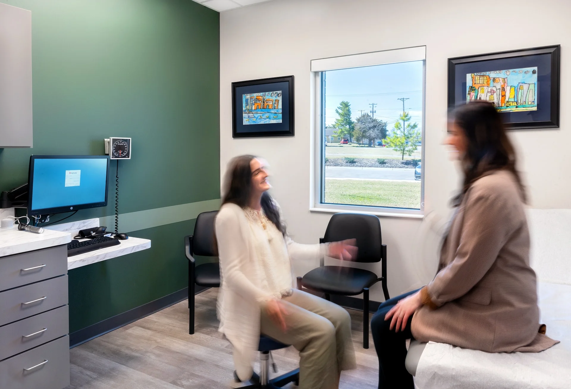 Patients interacting in a modern medical examination room at Summit Medical Group, featuring a computer station, clinical furnishings, and artwork, designed for efficient patient care and comfort, by George Ewart, a top commercial architect firm in Knoxville, TN.