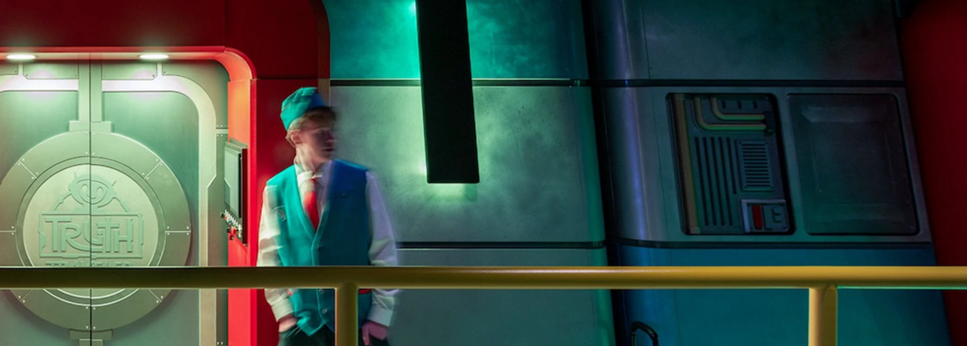 Person in a blue and green uniform standing near a metallic door labeled "TRUTH," set in a futuristic environment with vibrant lighting, showcasing design elements relevant to GAE Architecture + Design's athletic projects, designed and built by George Ewart, a top commercial architect firm in Knoxville, TN.