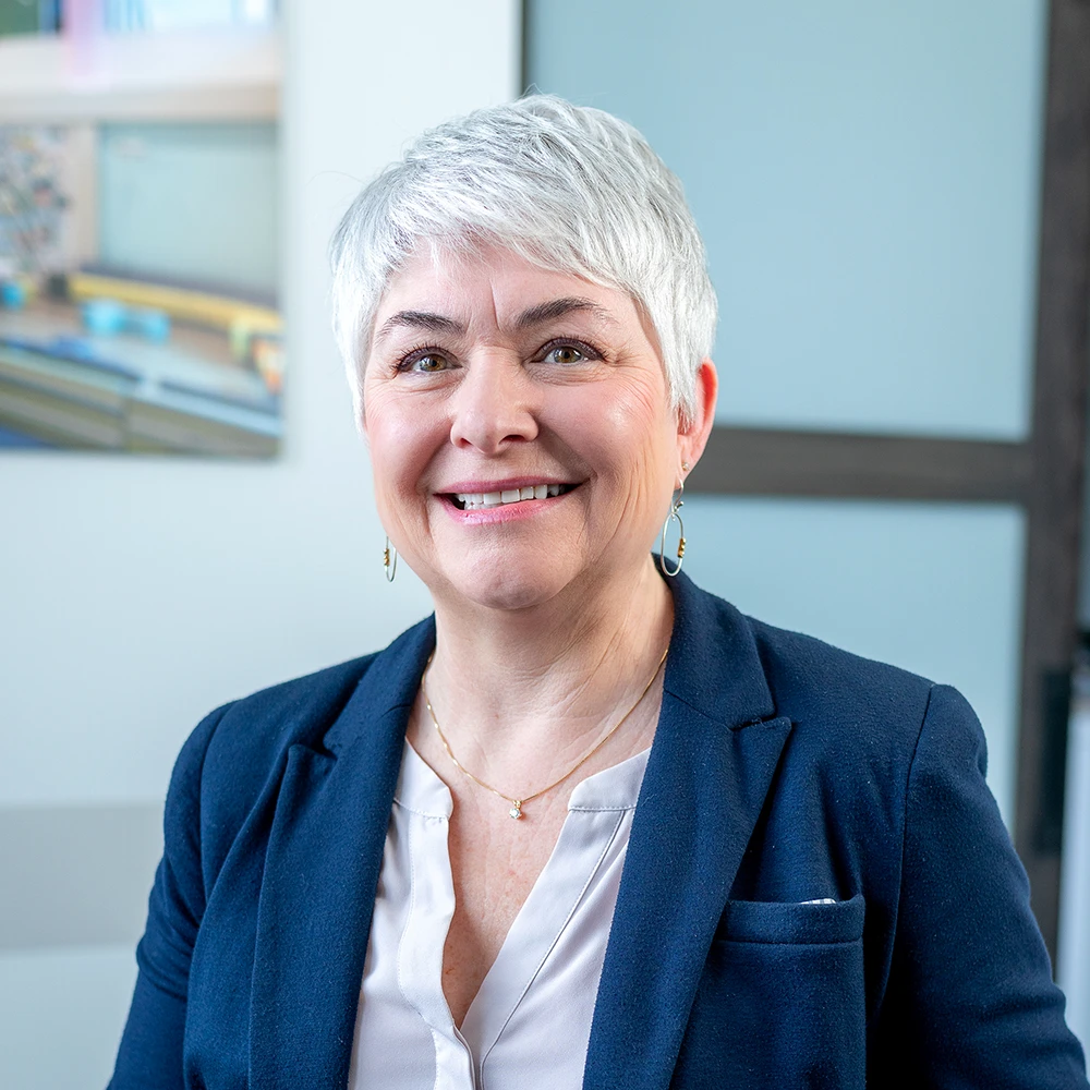 Cindy Ewart, office administrator at GAE Architecture + Design, smiling in a professional setting, showcasing her experience in management and administration.