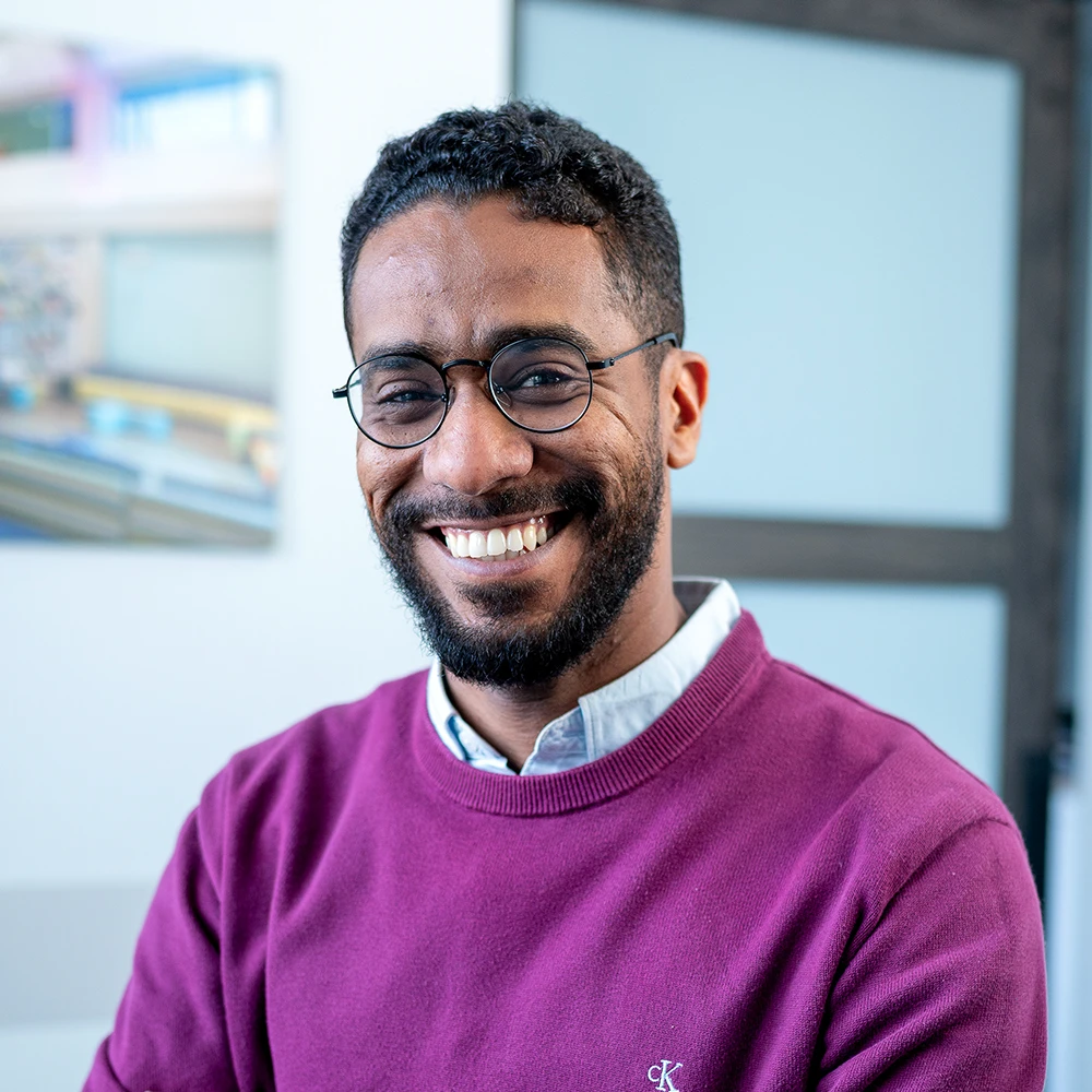 Munzir Shaikhoun, smiling architectural designer in a purple sweater, showcasing expertise in sustainable design at GAE Architecture + Design, Knoxville, TN.